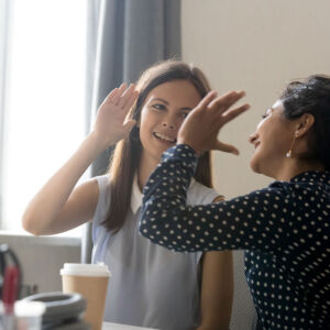 Coaching in Organizations with Ann Vanino - image of two women in business dress high giving at a work table