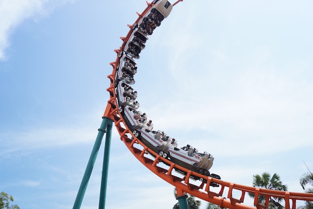 People on a curving red roller coaster against a blue sky